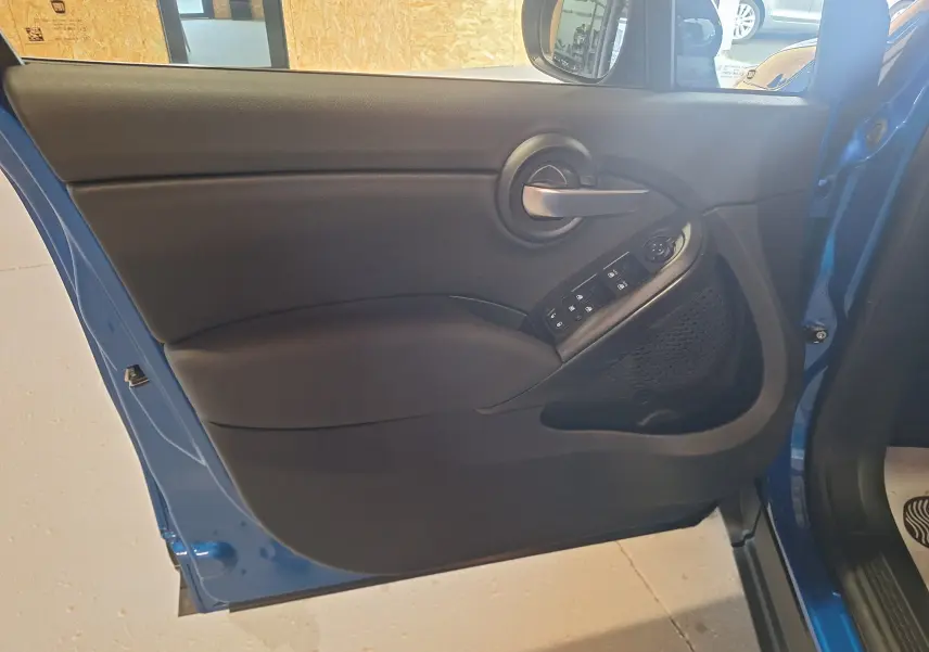 Vue intérieure de la porte avant gauche bleu métallisé du FIAT 500X 2024 avec commandes électriques et poignée grise.