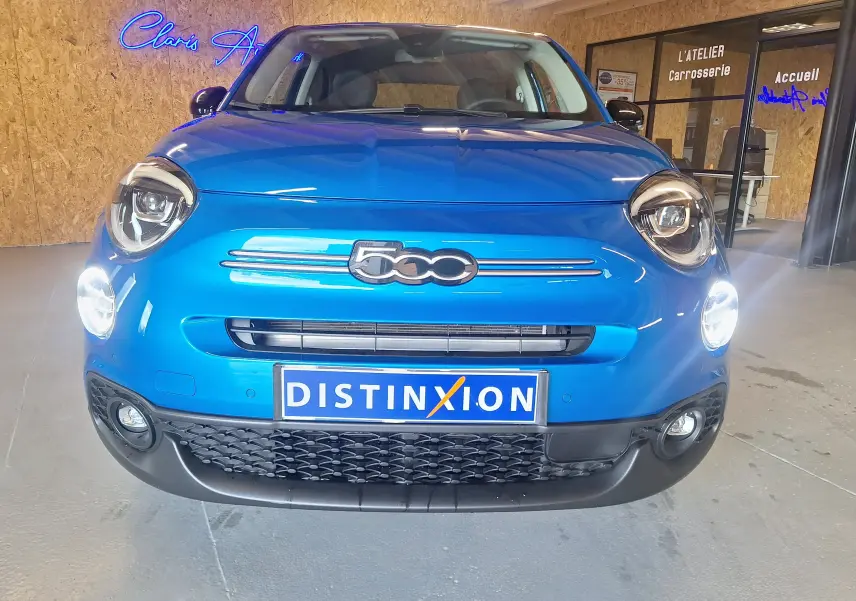 Vue frontale d'une FIAT 500X 2024 bleu métallisé avec phares allumés et logo distinctif 500 sur la calandre.