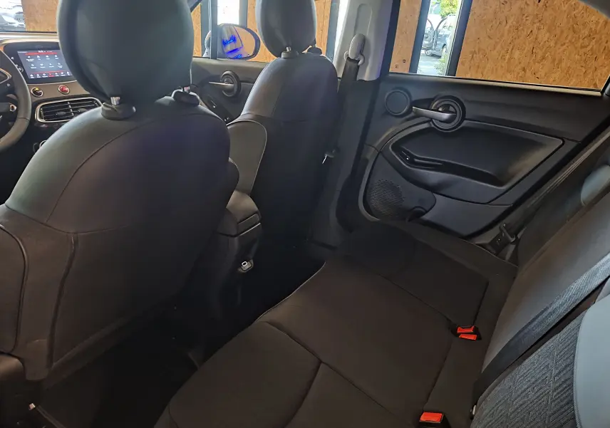 Vue intérieure arrière droite sur les sièges noirs et la portière du Fiat 500X bleu 2024 avec détails modernes.