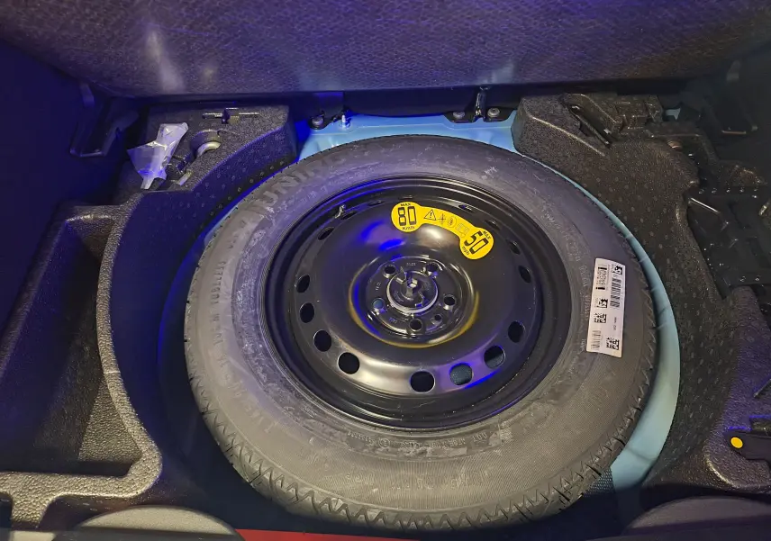 Pneu de secours noir dans le coffre bleu d'une Fiat 500X 1.5 Firefly 130 Sport Pack 2024 hybride essence.