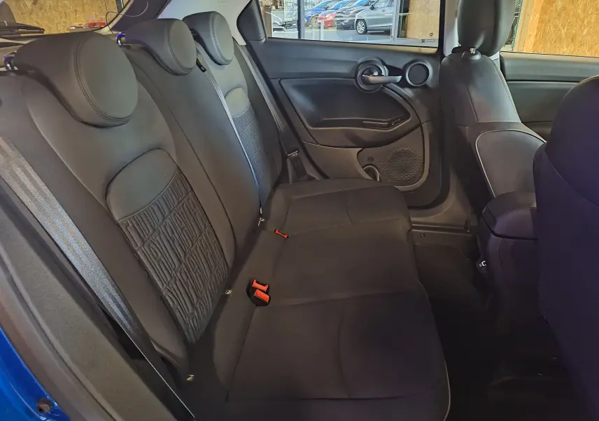 Vue intérieure côté droit sur la banquette arrière noire du FIAT 500X bleu 2024 avec appuie-têtes ronds et ceintures visibles.