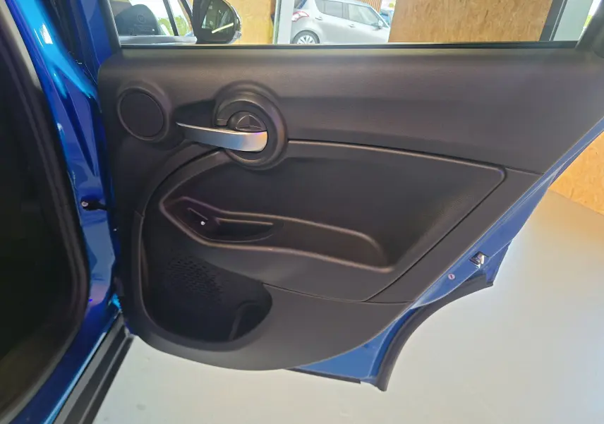 Porte arrière gauche ouverte de la FIAT 500X bleu 2024 montrant la garniture intérieure noire et la poignée argentée.