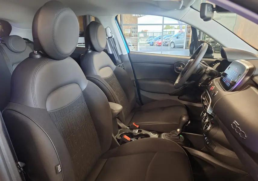 Intérieur avant de la FIAT 500X bleu 2024, sièges noirs avec logo, tableau de bord moderne et écran tactile central.