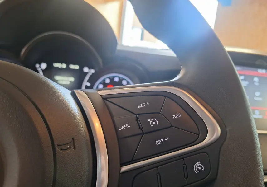 Gros plan sur les commandes du régulateur de vitesse au volant cuir de la FIAT 500X bleu 2024.