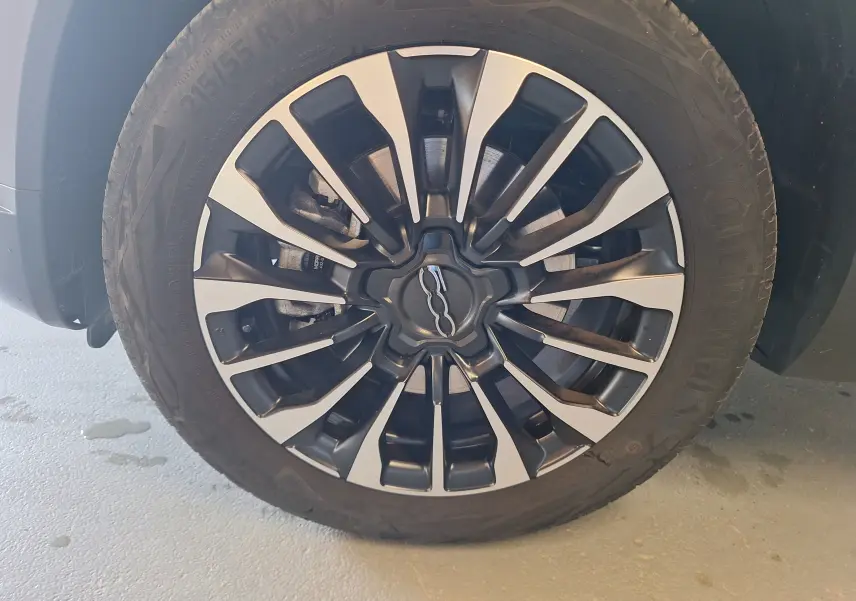 Gros plan sur la jante alliage bicolore avec logo FIAT 500 au centre du SUV bleu FIAT 500X 2024.