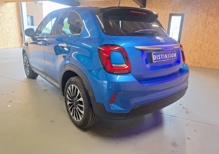Vue 3/4 arrière droite d'un FIAT 500X bleu métallisé avec jantes alliage et feux arrière LED dans un garage.