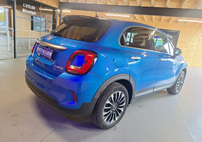 Vue 3/4 arrière droite d'une FIAT 500X 2024 bleu métallisé avec logo Hybrid et jantes alliage distinctives.