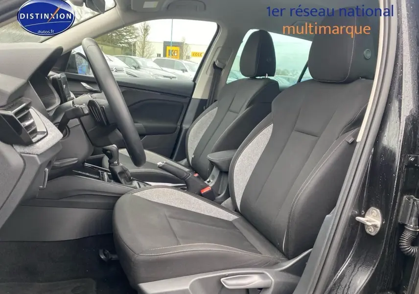 Vue intérieure côté conducteur du Skoda Kamiq noir 2025, sièges tissu bicolore avec accoudoir central et volant cuir multifonction.