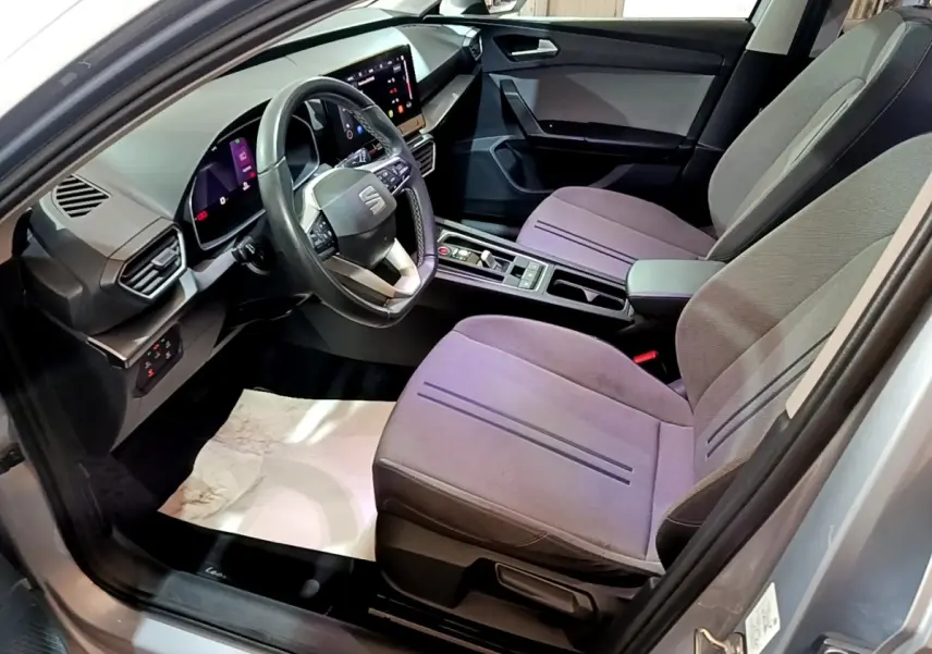 Vue intérieure côté conducteur de la SEAT Leon gris foncé 2022, avec tableau de bord digital et sièges tissu gris.