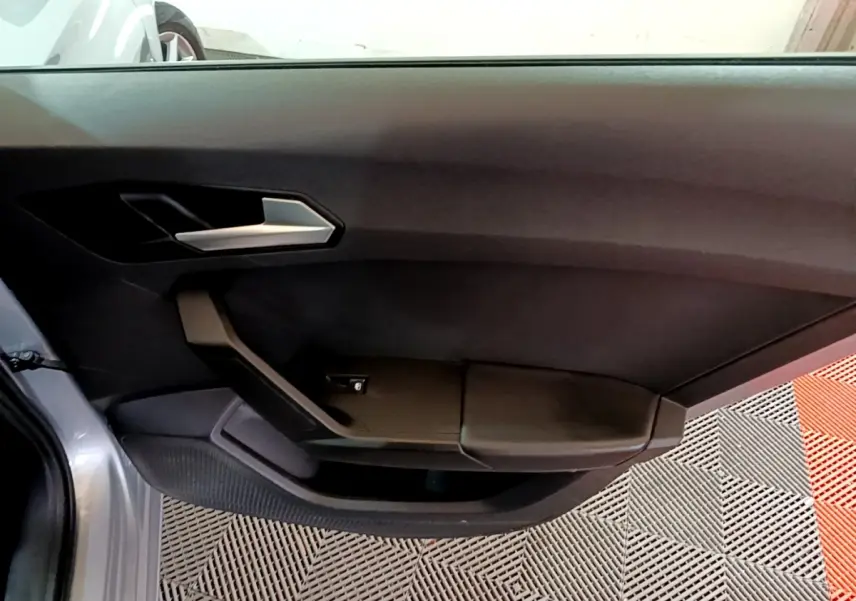Vue rapprochée de la porte avant gauche grise foncée du SEAT LEON 2022, avec poignée argentée et accoudoir noir.