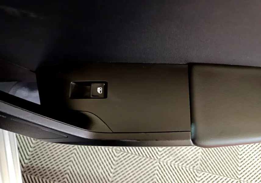Détail du bouton d'ouverture de coffre sur l'accoudoir intérieur côté conducteur d'une SEAT Leon gris foncé.