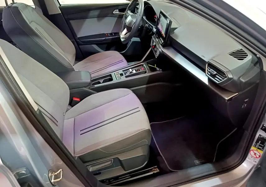 Intérieur avant de la SEAT Leon gris foncé, vue côté conducteur, avec écran tactile central et sièges tissu gris.