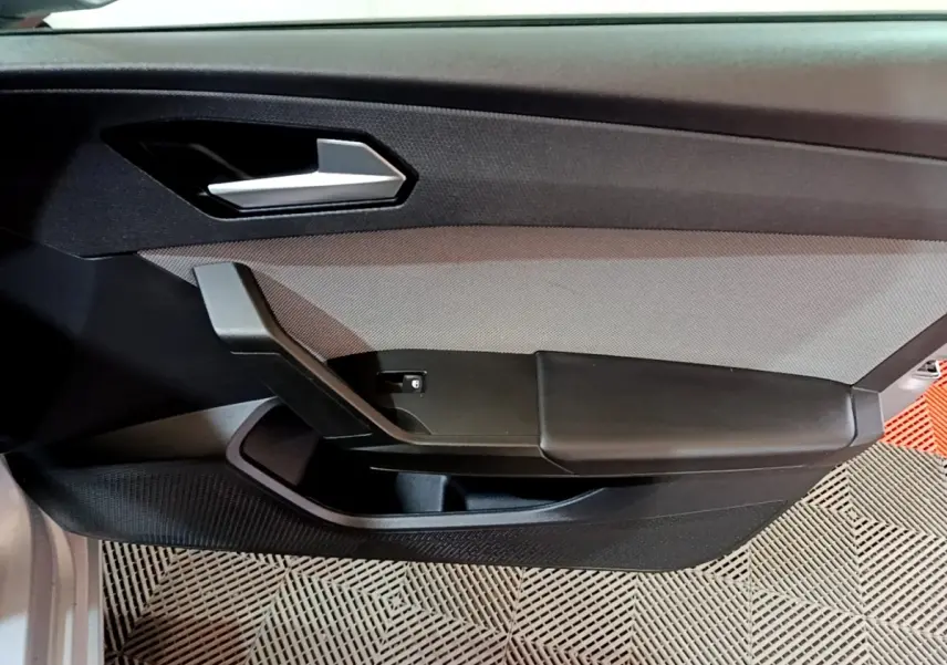 Vue intérieure côté gauche de la porte avant gris foncé de la SEAT LEON 2022 avec poignée argentée et accoudoir noir.