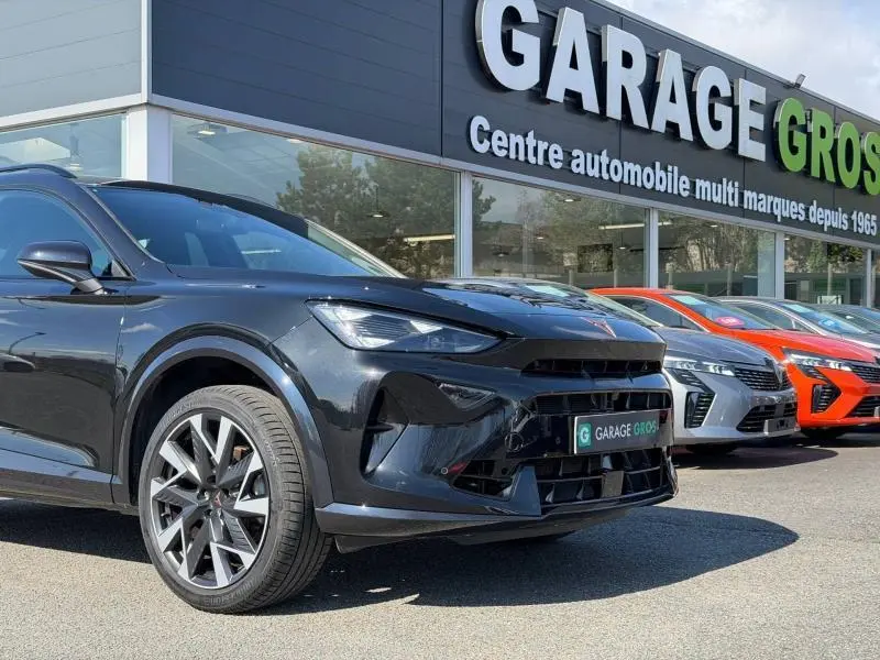 Vue 3/4 avant gauche d'une CUPRA Formentor 1.5 eTSI Hybrid noire métallisée, devant un garage multimarques.