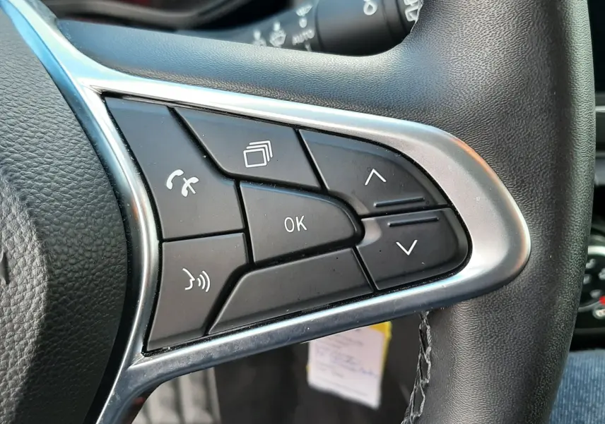 Gros plan sur les commandes multifonctions à droite du volant noir de la Renault Clio V blanche, tableau de bord en arrière-plan.