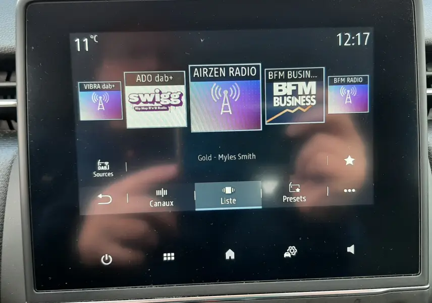 Écran tactile central de la Renault Clio V blanc, affichant les stations radio numériques avec commandes en dessous.