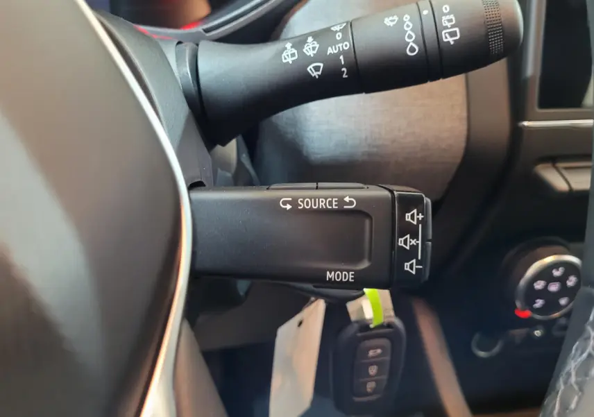 Gros plan sur la commande multifonctions à gauche du volant de la Renault Clio bleu, avec boutons source et mode visibles.