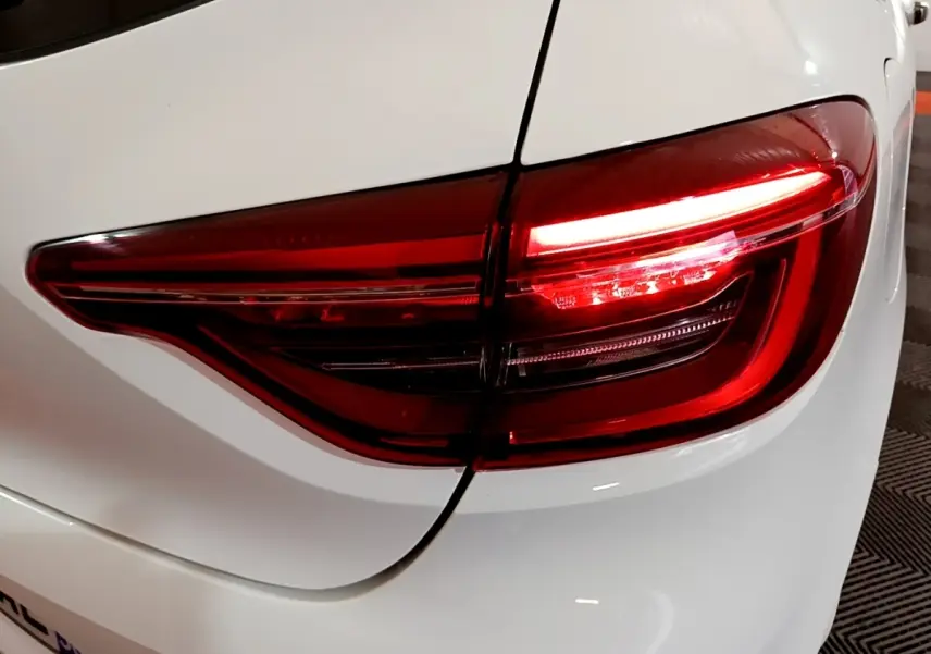 Gros plan sur le feu arrière droit rouge d'une Renault Clio Business blanche, soulignant la carrosserie lisse et brillante.