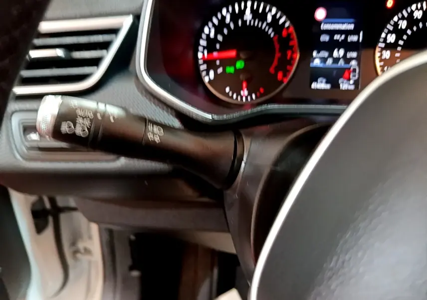 Gros plan sur le commodo de clignotant noir et le tableau de bord éclairé de la Renault Clio Business blanche de 2021.