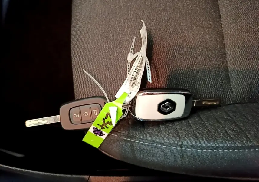 Clés de voiture Renault posées sur un siège en tissu gris foncé, sans vue du véhicule.