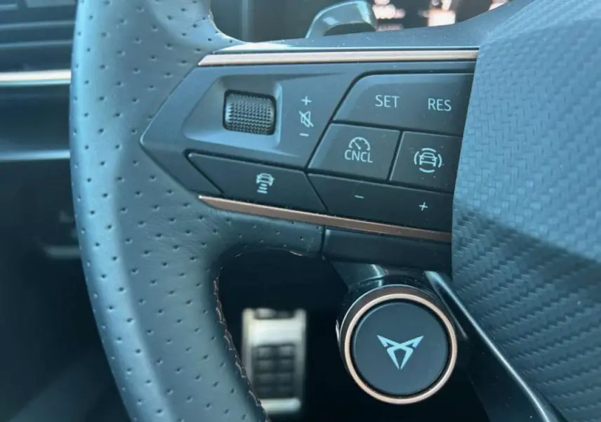 Gros plan sur le volant perforé du CUPRA Formentor blanc 2025, avec commandes intégrées et logo distinctif au centre.