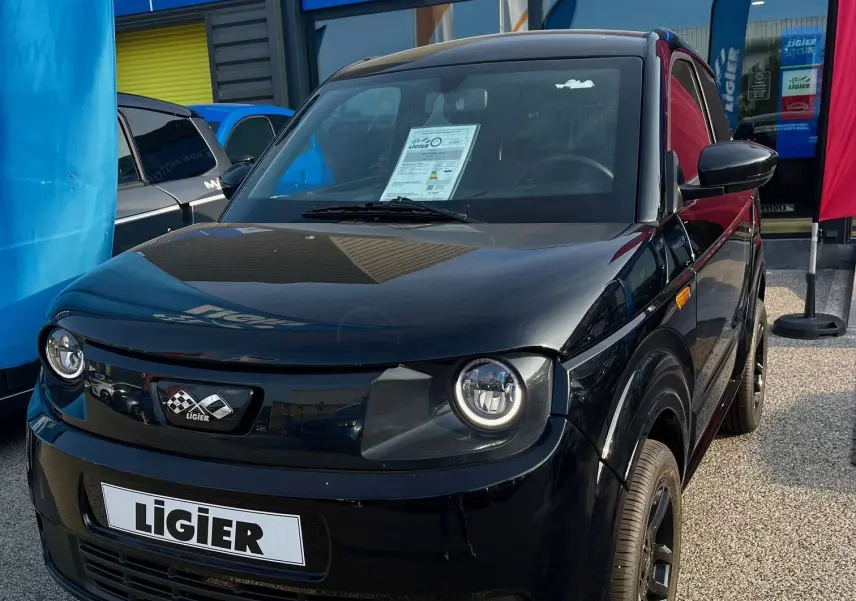 Vue 3/4 avant d'une Ligier Myli I.DEL 8KWH noire intense garée devant un magasin Ligier Store.