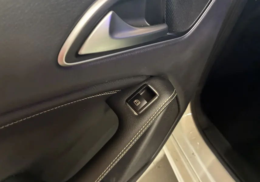 Gros plan sur la poignée intérieure et le bouton de lève-vitre côté conducteur d'une Mercedes Classe A blanche de 2016.