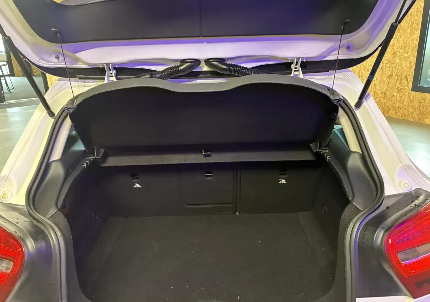 Coffre ouvert vu de l'arrière d'une Mercedes Classe A 200D blanche, montrant l'espace de chargement vide et la tablette cache-bagages relevée.