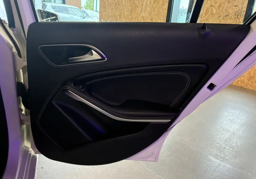 Vue intérieure de la porte arrière gauche d'une Mercedes Classe A 200D blanche, garniture cuir noir avec surpiqûres blanches.