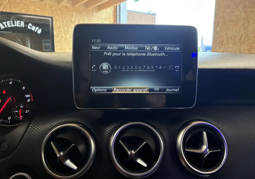 Écran central tactile et trois aérateurs ronds sur le tableau de bord noir d'une Mercedes Classe A 200D 2016.