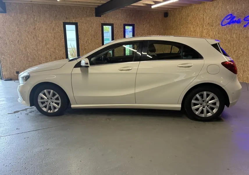 Profil côté gauche d'une Mercedes Classe A 200D blanche de 2016, compacte avec cinq portes, dans un garage éclairé.