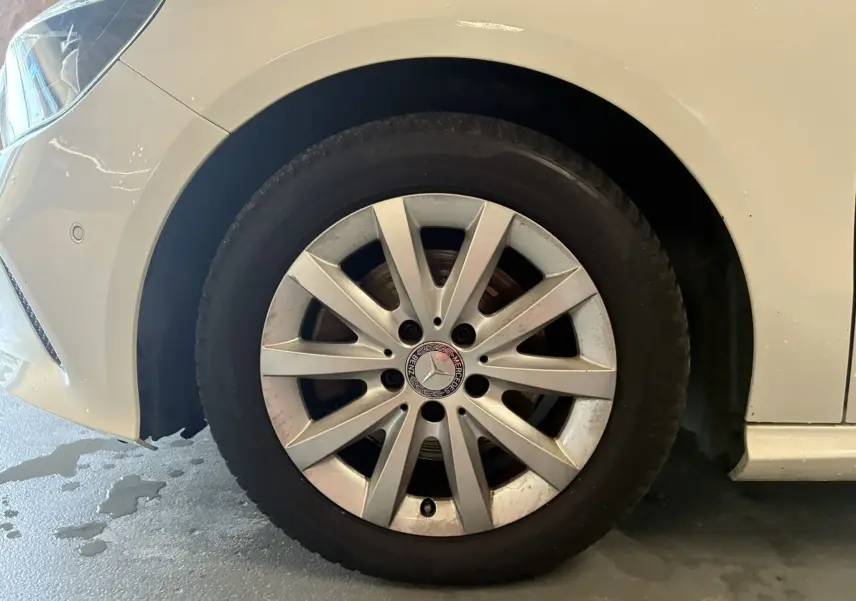 Gros plan sur la roue avant gauche d'une Mercedes Classe A blanche, mettant en valeur la jante alliage et le logo central.