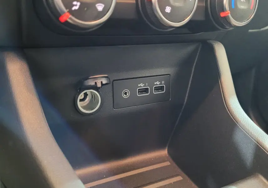 Gros plan sur la console centrale noire de la Renault Clio avec prise 12V et deux ports USB visibles.