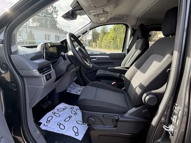 Vue intérieure côté conducteur du Volkswagen Transporter T7 ProCab Business 2026 en graphite dust, avec tableau de bord moderne et sièges tissu noirs.