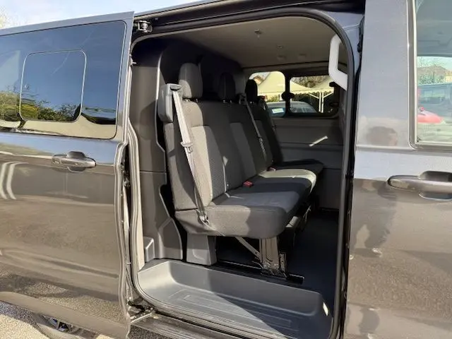 Vue latérale droite du Volkswagen Transporter T7 ProCab graphite dust avec porte coulissante ouverte, montrant les sièges arrière en tissu gris.