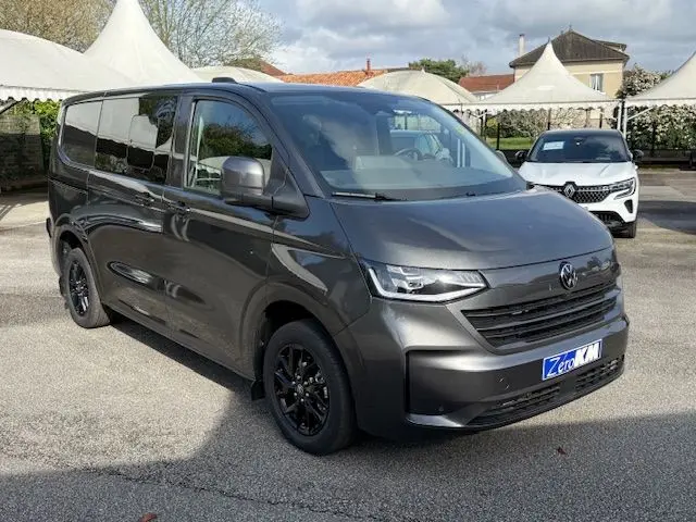Vue 3/4 avant droit d’un Volkswagen Transporter T7 ProCab Business gris graphite avec jantes noires, stationné en extérieur.