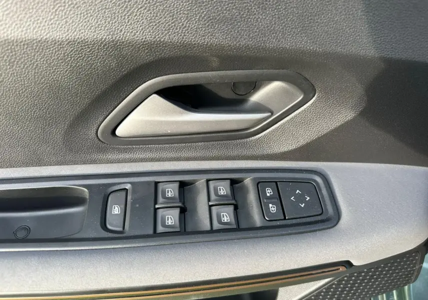 Gros plan sur la commande des vitres électriques et poignée intérieure côté conducteur de la Dacia Sandero III Stepway vert cèdre.