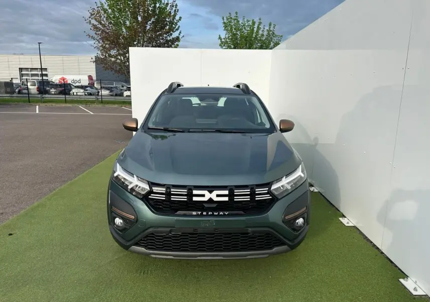 Vue avant d'une Dacia Sandero III Stepway vert cèdre avec calandre noire et détails brun cuivré sur pare-chocs et rétroviseurs.