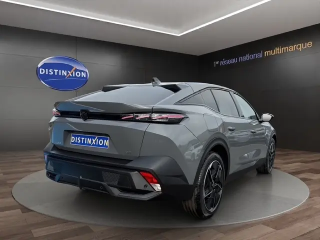 Vue 3/4 arrière droite d’une Peugeot 408 Hybrid 145 e-DCS6 GT gris clair en showroom avec feux arrière LED fins.