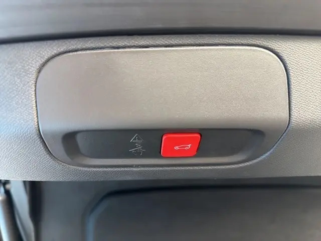 Gros plan sur le bouton rouge d'ouverture électrique du coffre dans un Peugeot 408 Hybrid gris clair, intérieur noir.