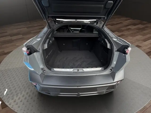Coffre ouvert en vue arrière d'une Peugeot 408 Hybrid gris clair, montrant l'espace de chargement vide et la trappe à skis.
