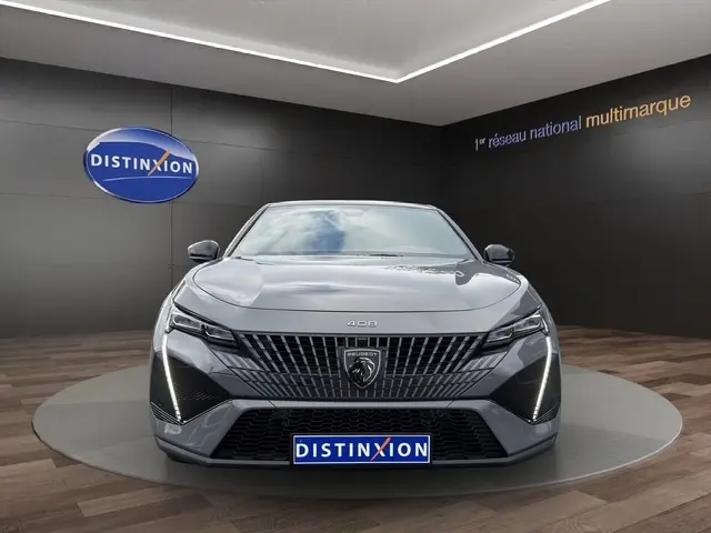 Vue frontale d'une Peugeot 408 Hybrid 145 e-DCS6 GT gris clair avec feux LED et calandre distinctive en showroom.