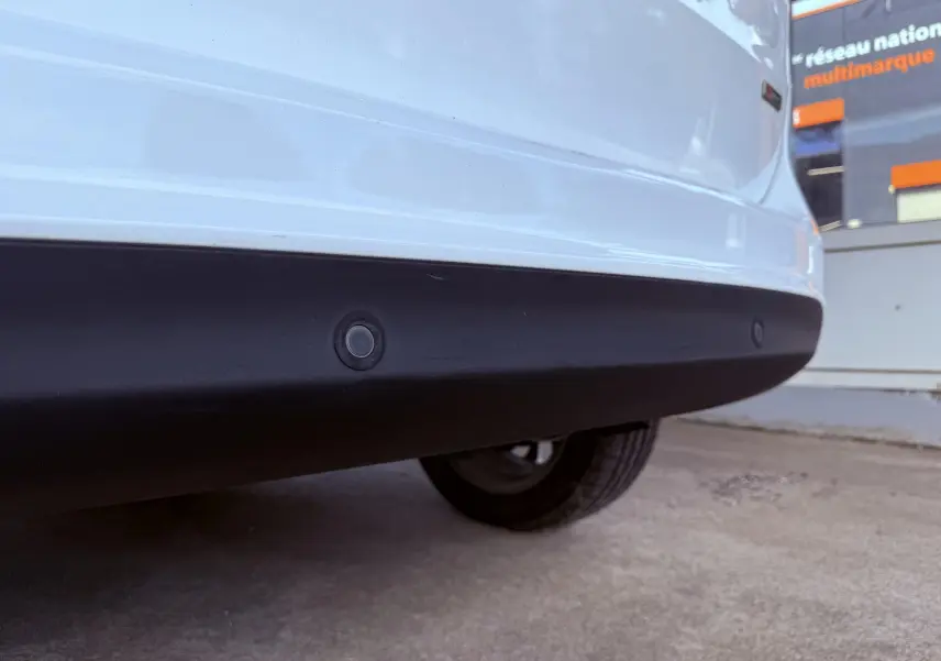 Gros plan sur le pare-chocs arrière blanc d'une Ford B-MAX 2014 avec capteurs de recul visibles sur fond noir.