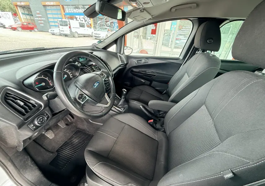 Vue intérieure côté conducteur de la Ford B-MAX 2014, sièges tissu gris et volant multifonction noir.