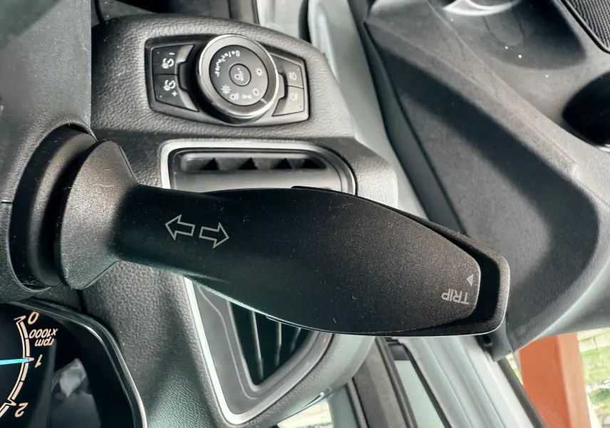 Gros plan sur la manette de clignotant noir dans l'habitacle d'une Ford B-MAX blanche, avec commandes d'éclairage en arrière-plan.