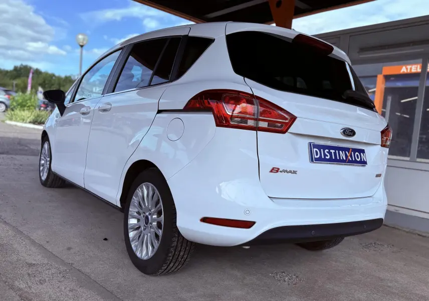 Vue 3/4 arrière gauche d'une Ford B-MAX blanche stationnée sous un abri avec jantes alliage visibles.