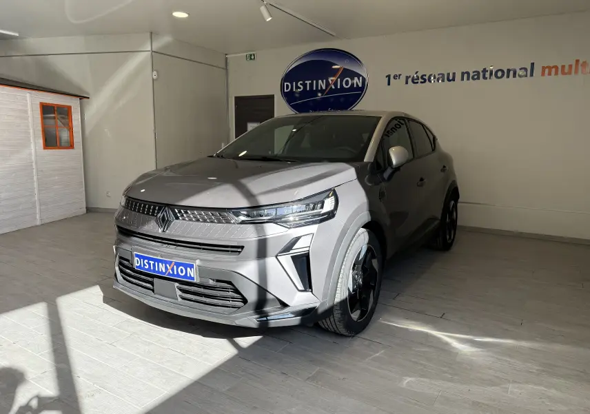 Renault Captur 2025 gris cassiopée métal avec toit gris, vue 3/4 avant droit en intérieur showroom lumineux.
