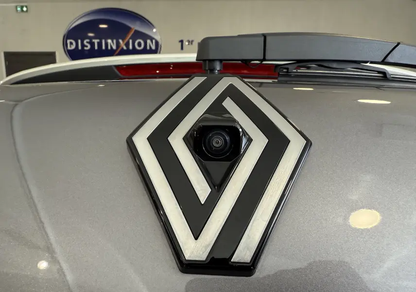 Gros plan sur le logo Renault gris métallisé avec caméra intégrée sur un Renault Captur 2025 gris Cassiopée.