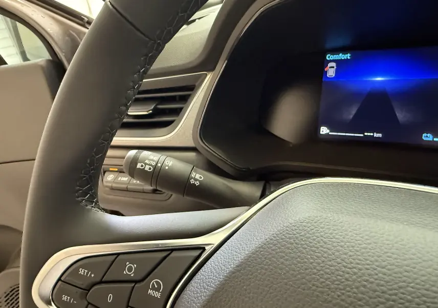 Gros plan sur le volant et le tableau de bord numérique bleu du Renault Captur gris Cassiopée, version hybride 2025.