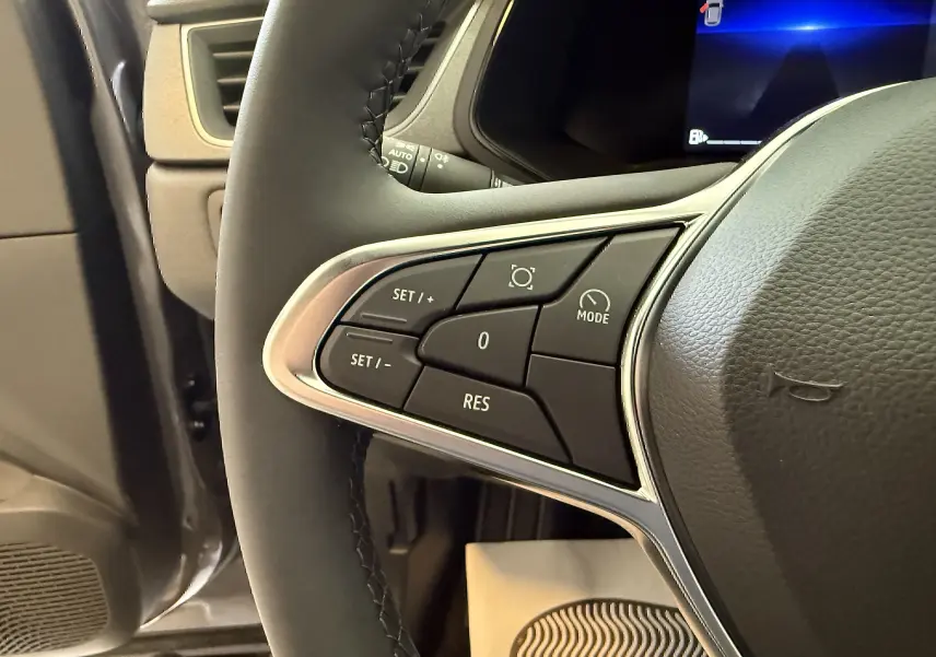 Gros plan sur les commandes gauche du volant d’un Renault Captur gris Cassiopée, affichage digital en arrière-plan.